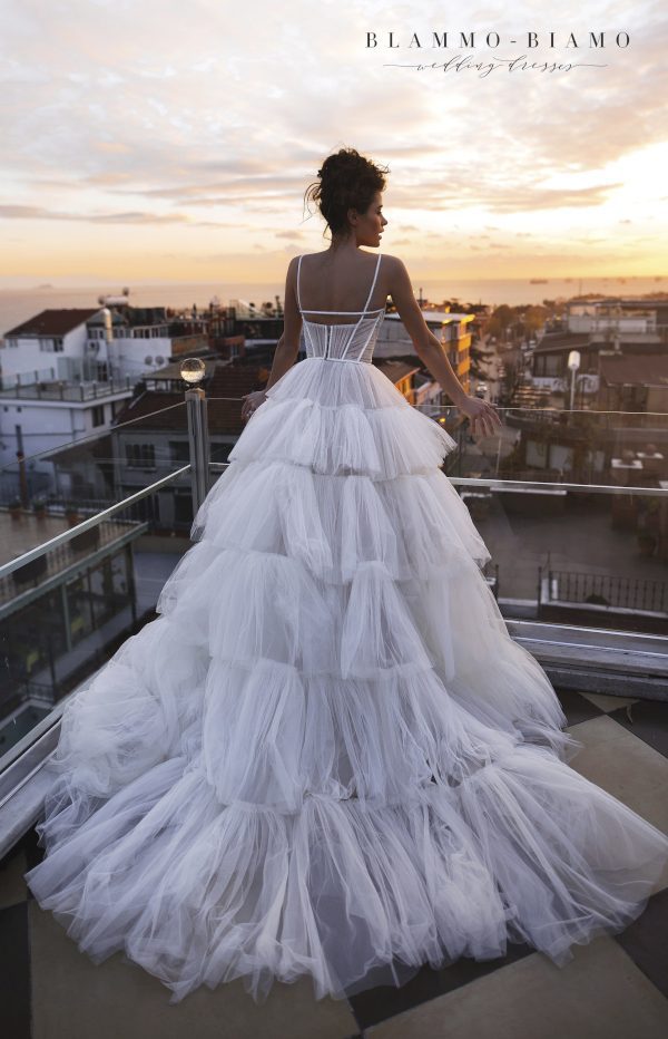 A bride wearing princess wedding dress Liam by Blammo-Biamo with fluffy multi-layered skirt and bodice embroidered with ribbons, back view.