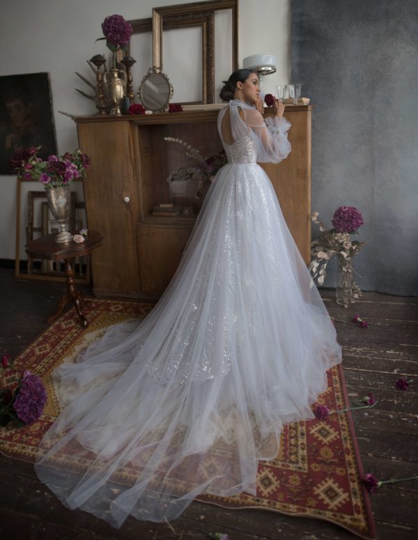 A bride wearing wedding A-line dress with lush skirt made of sequin fabric with a long train and bodice decorated with beadings, back view.