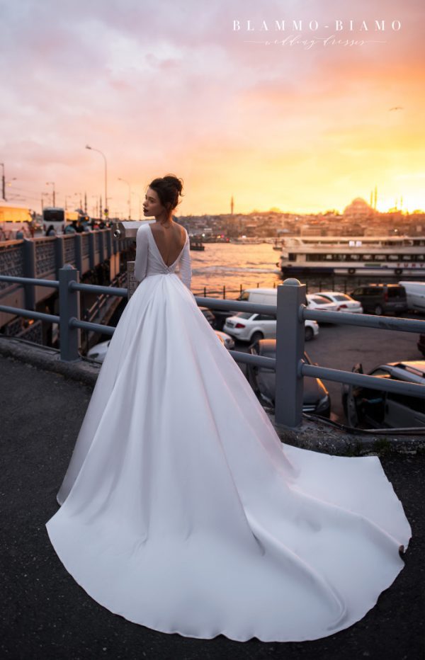 A bride wearing satin princess wedding dress Tilda by blammo-biamo with long sleeves, long train and open back with brooch, image 2