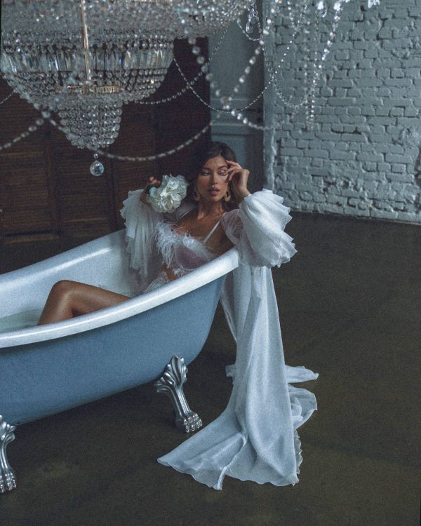 A bride sitting in a bath and wearing a white bridal robe Kim by rara avis with sleeves